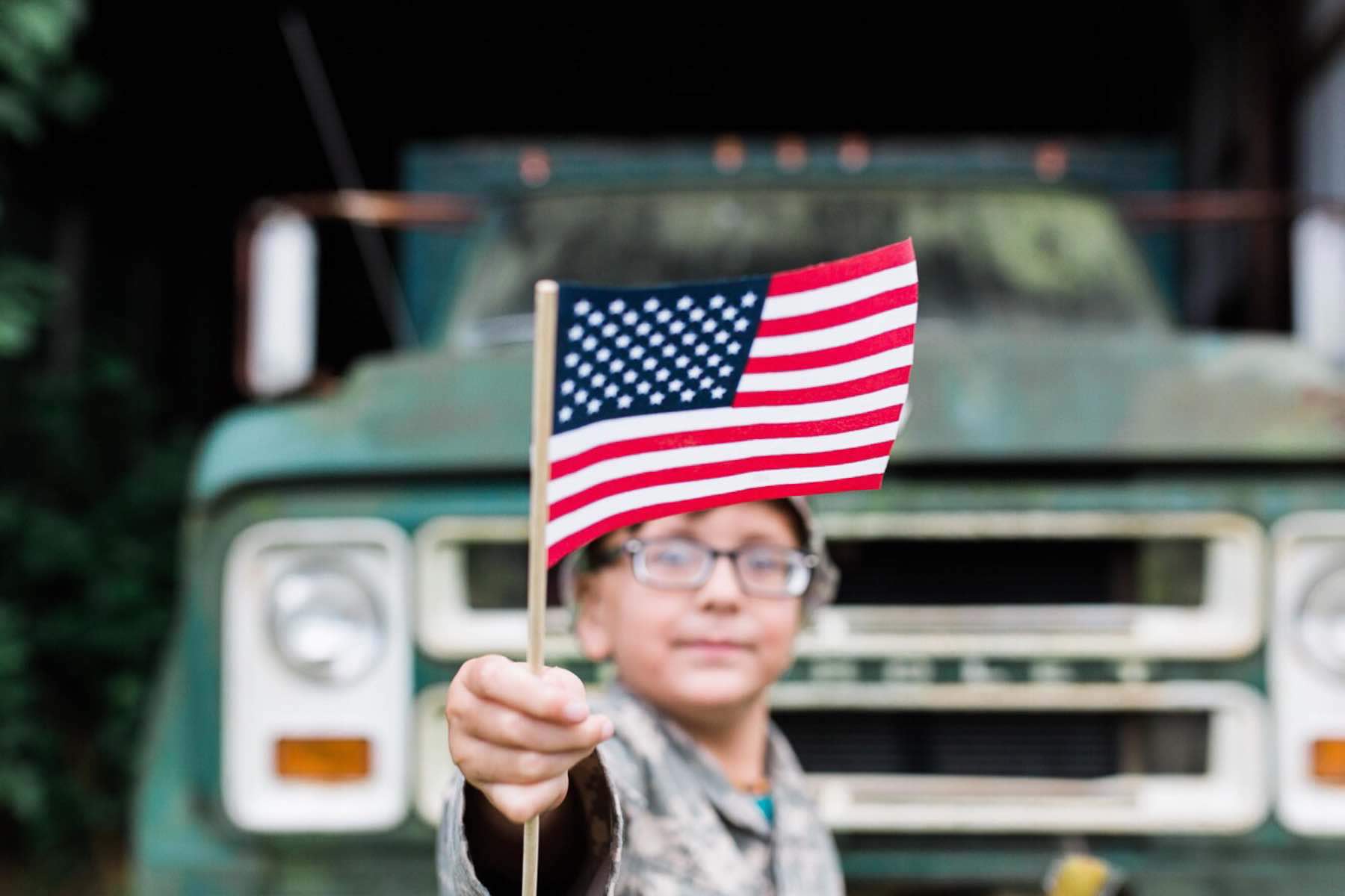 Child holding american flag in front of a truck