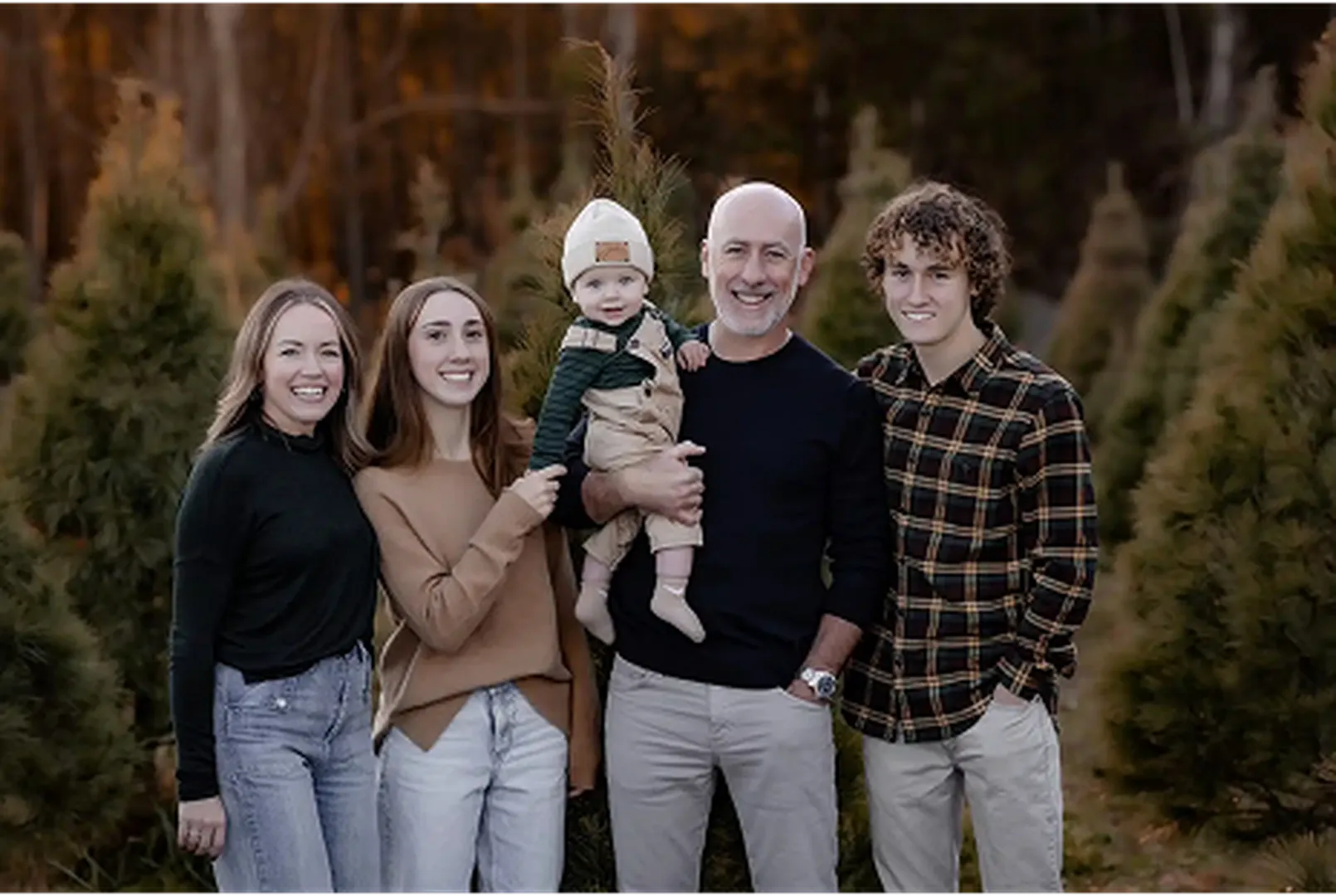 A family group stands together in a forested area, sharing a joyful moment in casual attire.