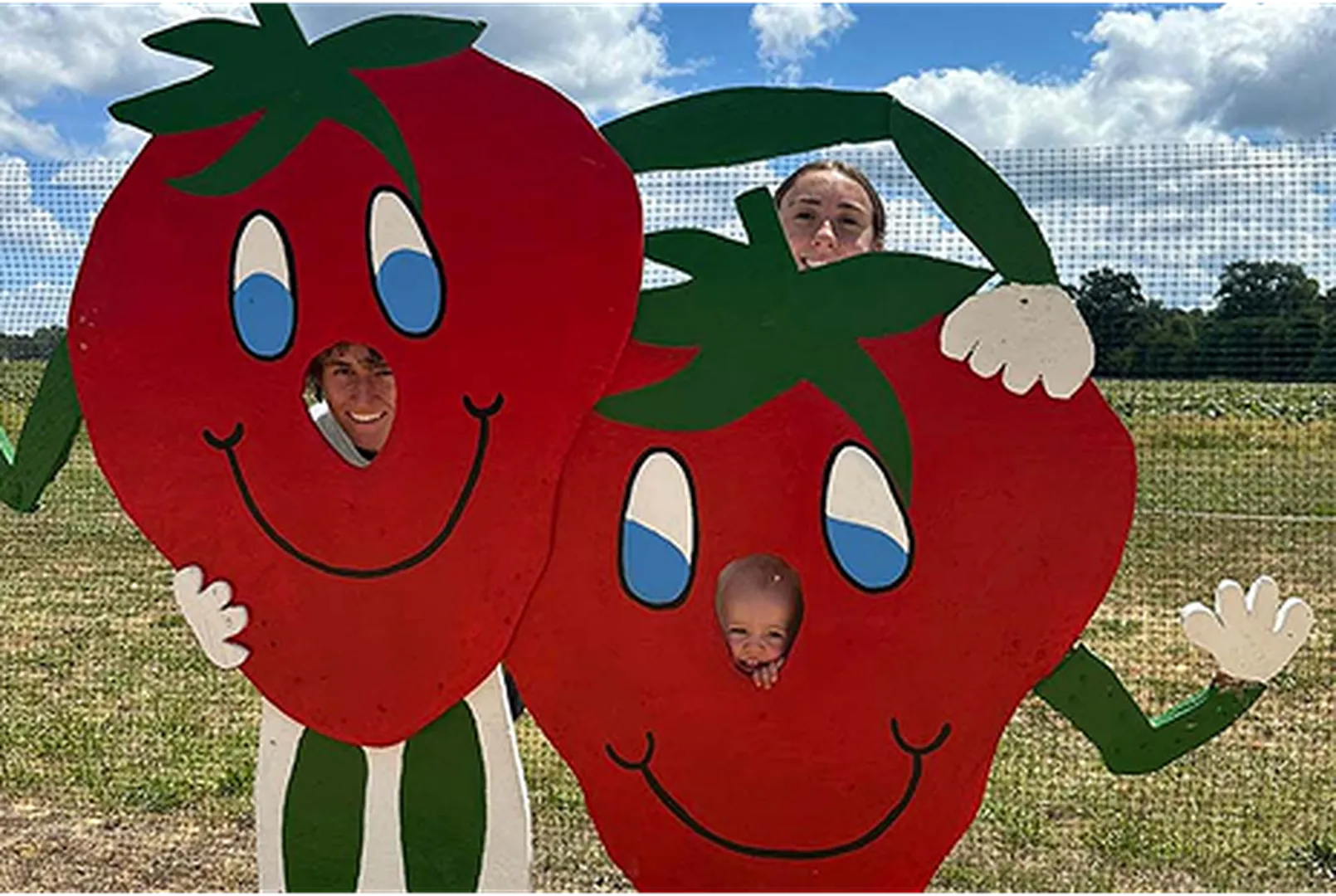A girl holding two cartoon strawberry cutouts with green leafy hats in a field.