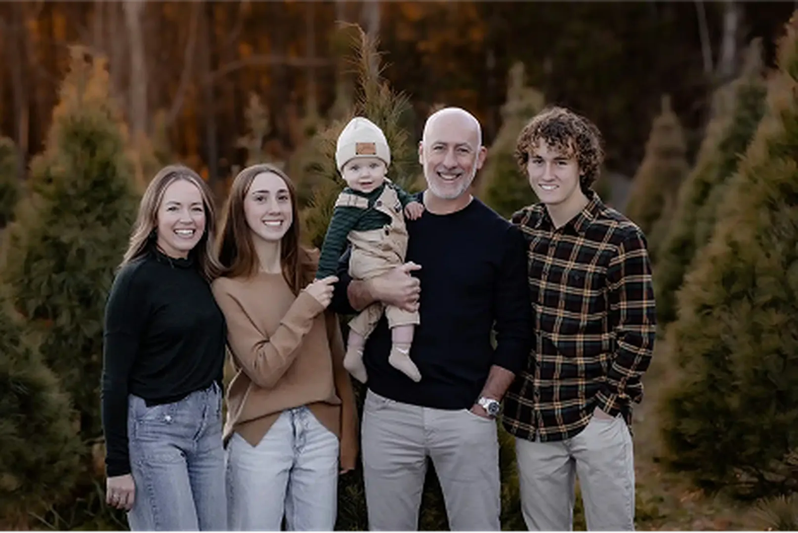 A family group stands together in a forested area, sharing a joyful moment in casual attire.