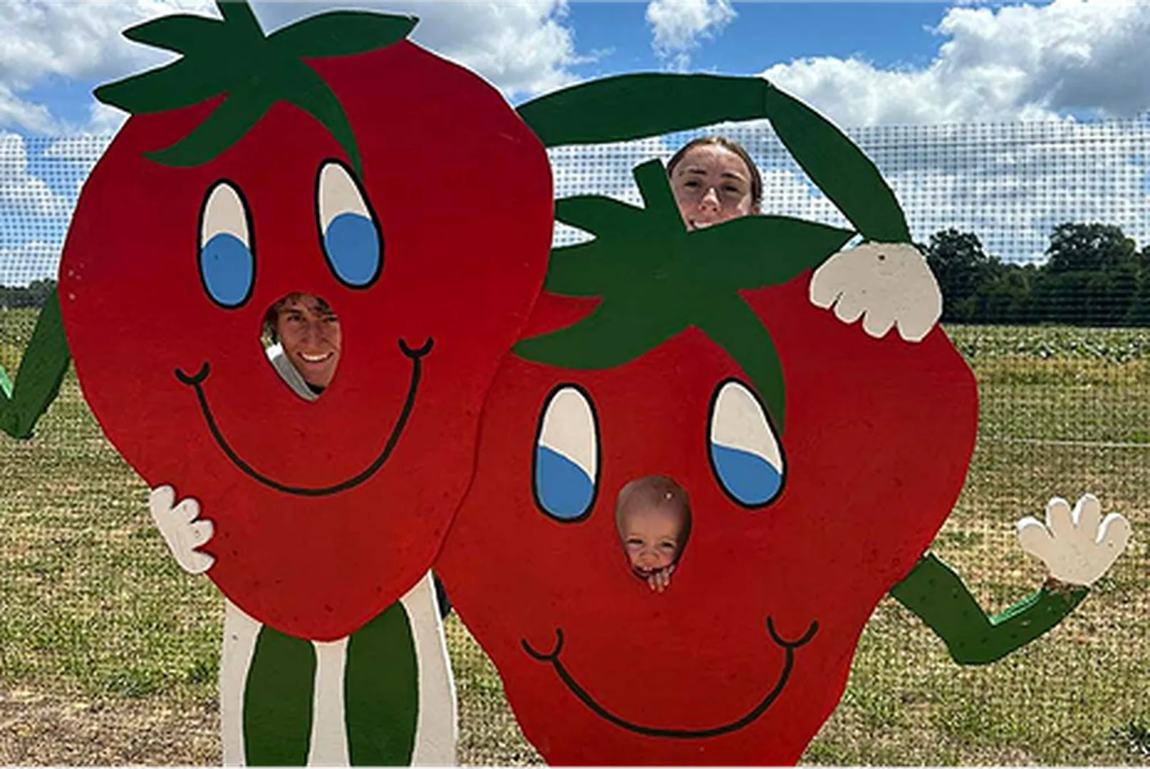 A girl holding two cartoon strawberry cutouts with green leafy hats in a field.